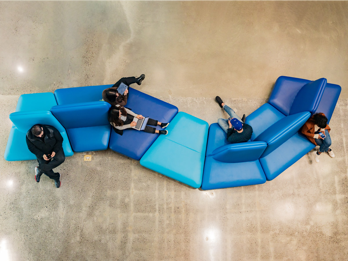 A bird's-eye view of students resting and working on a long, curved blue couch.