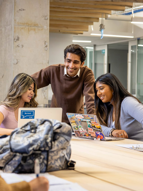 A group of students laugh as they share something on their laptop screens.