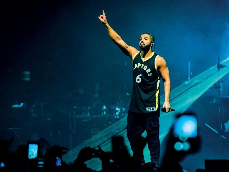 Drake, Musical Artist, on stage performing his music with people's hands in the air below the stage.