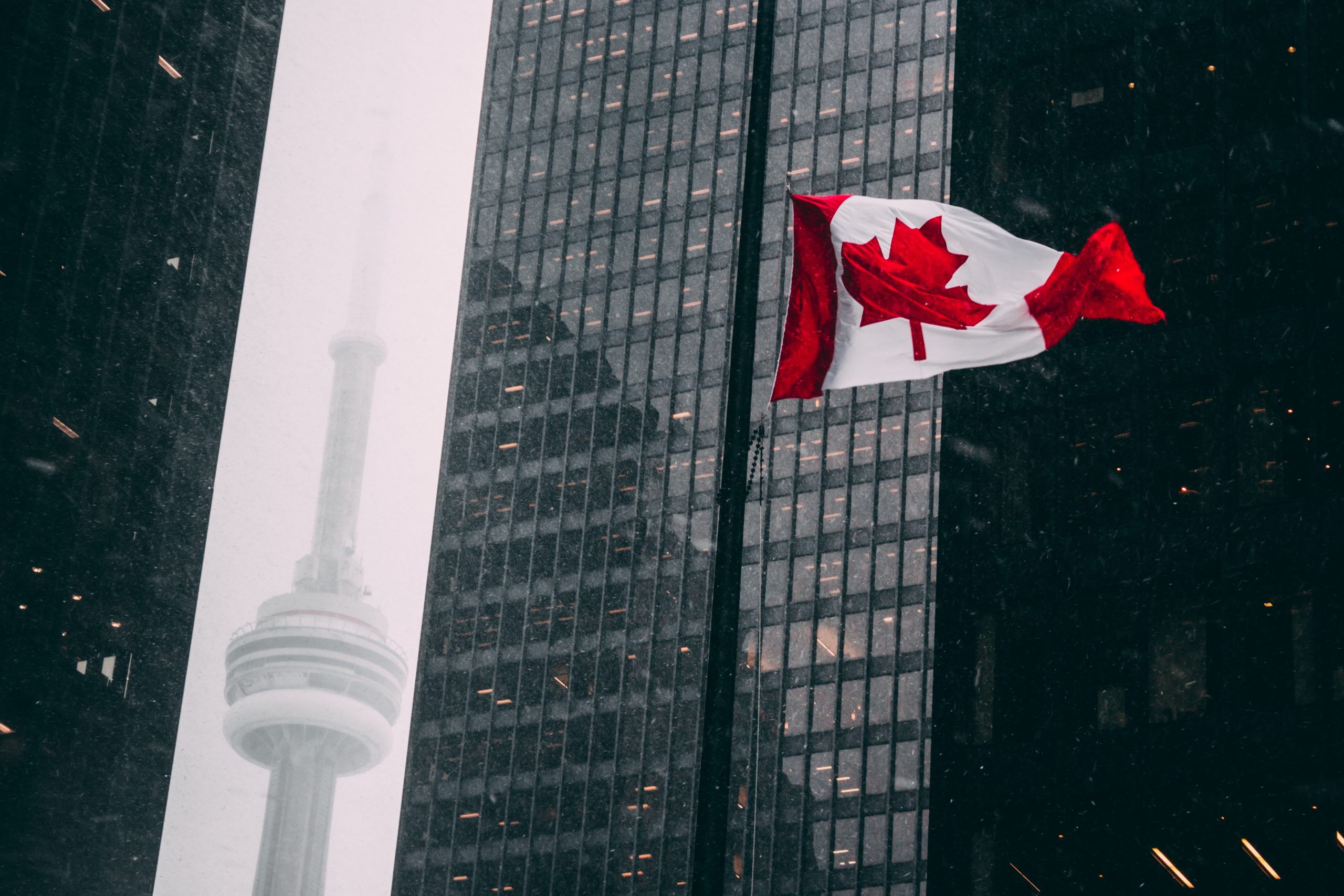 Dramatic photo of the Canadian flag and CN Tower from the financial district in Toronto
