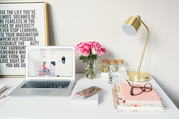 Desk that contain laptop, notebook, glasses, poster and a lamp