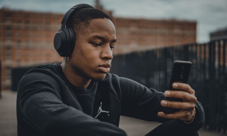 Younge male looking at their phone with headphones on.