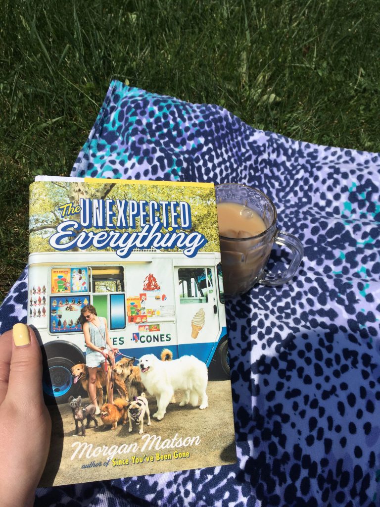 Holding a book, while sitting on a blanket with coffee on grass