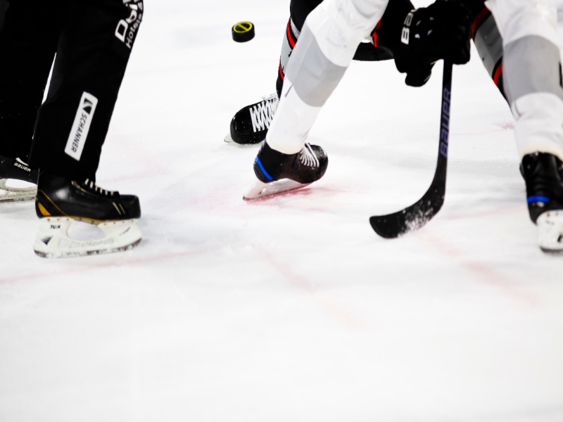 Close up picture of 2 people playing hockey with a visible stick and puck