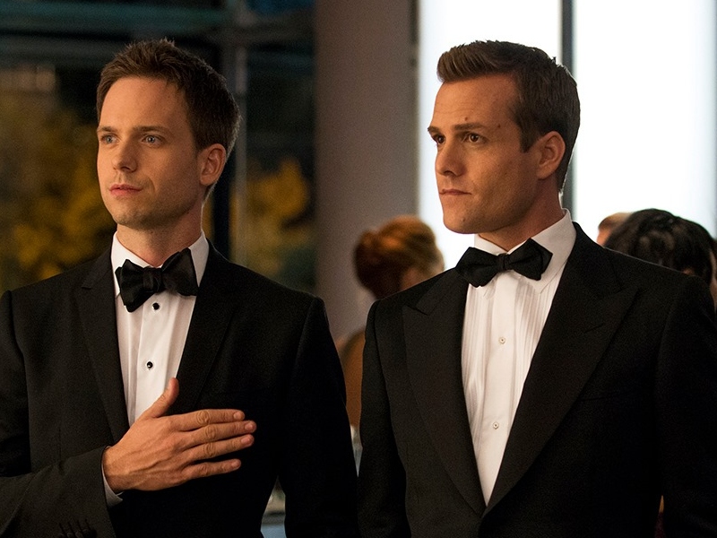 Harvey Specter and Mike Ross standing in a photo wearing suits as the main characters of the show Suits