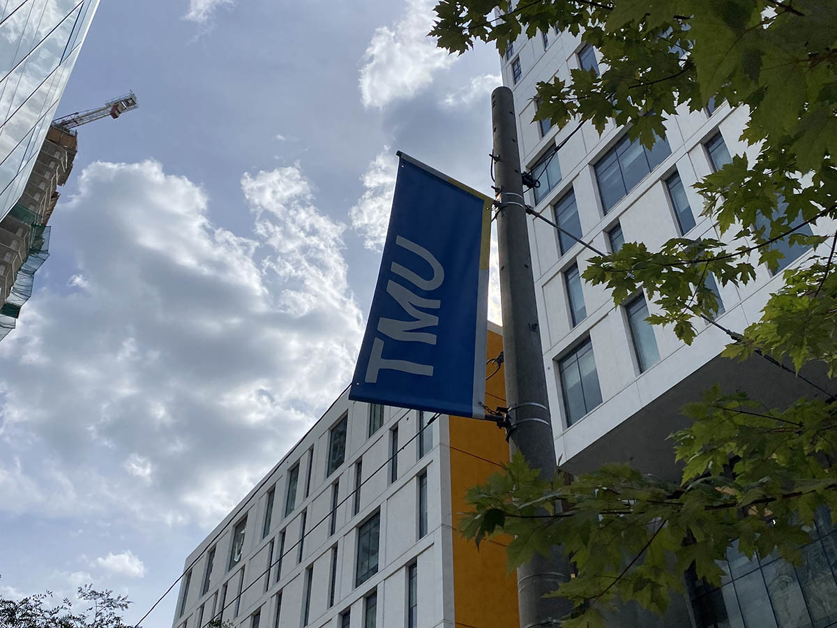 A TMU banner waves on a street pole in front of the Daphne Cockwell Complex on the TMU campus.