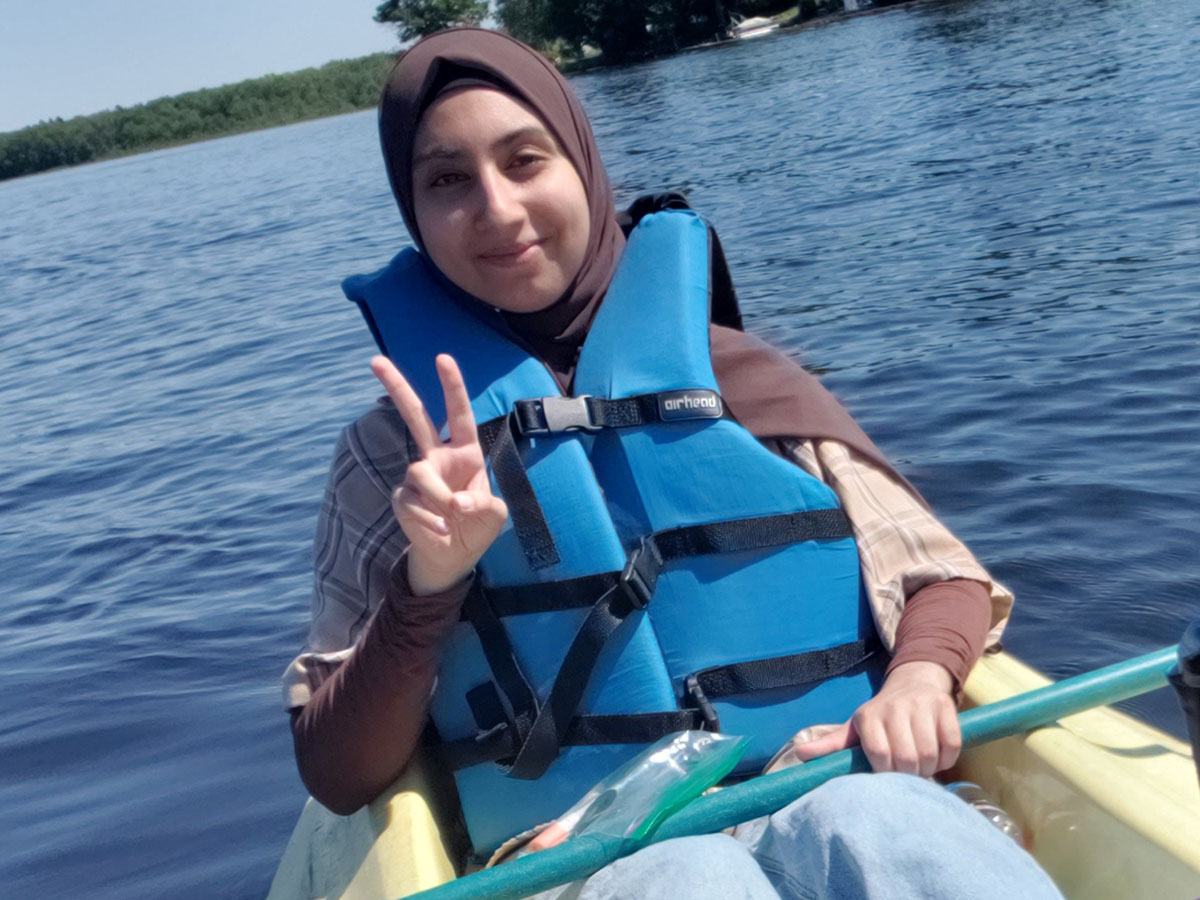 Saba smiles and gives a peace sign while canoeing during a Student Group Leadership Retreat.