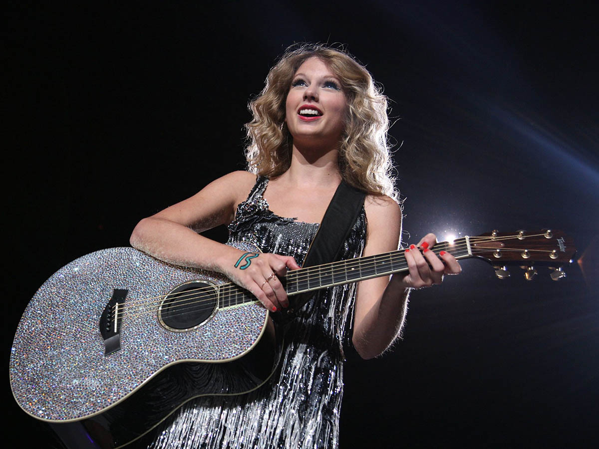 Taylor Swift performing with a glittery, silver guitar with a number 13 painted on her hand during her "Fearless" era. 