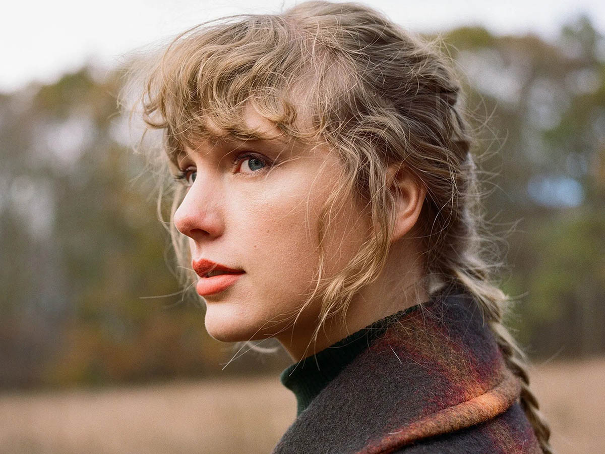 Taylor Swift with braided hair and a plaid shirt in a field for an "evermore" photoshoot.