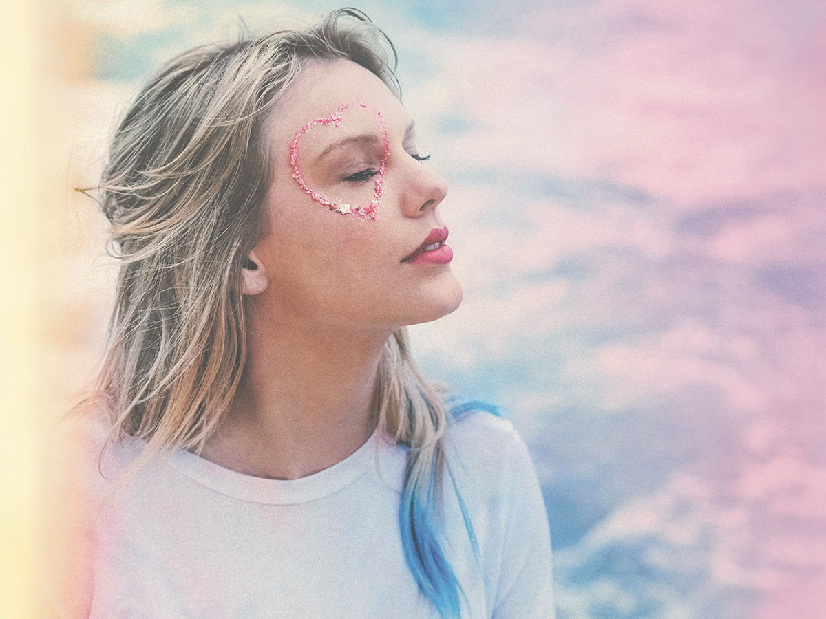 Taylor Swift in front of a pastel background with a glitter heart around her eye during her "Lover" era.