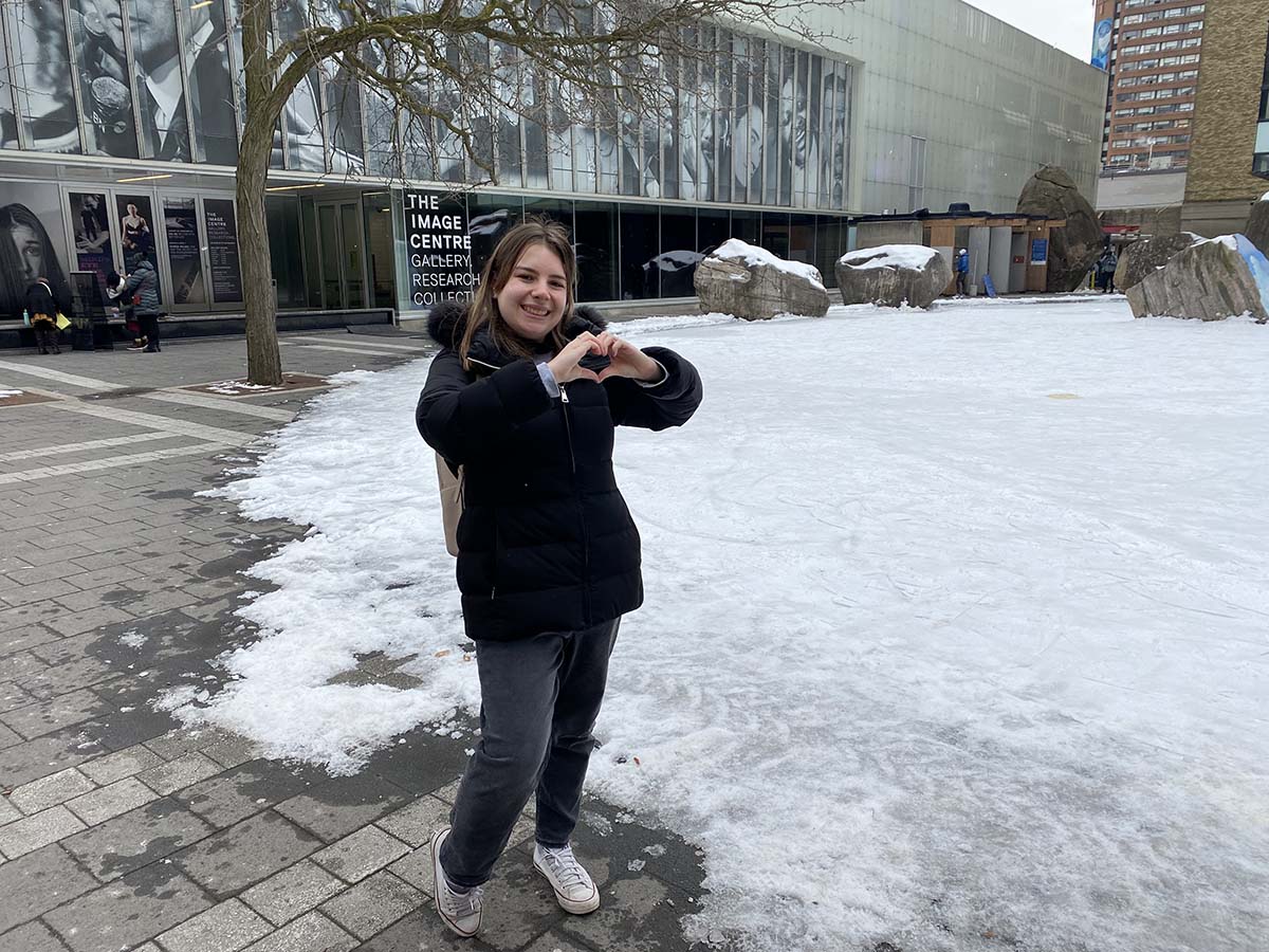 Jenna making a heart with her hands in front of a snow-covered Lake Devo.