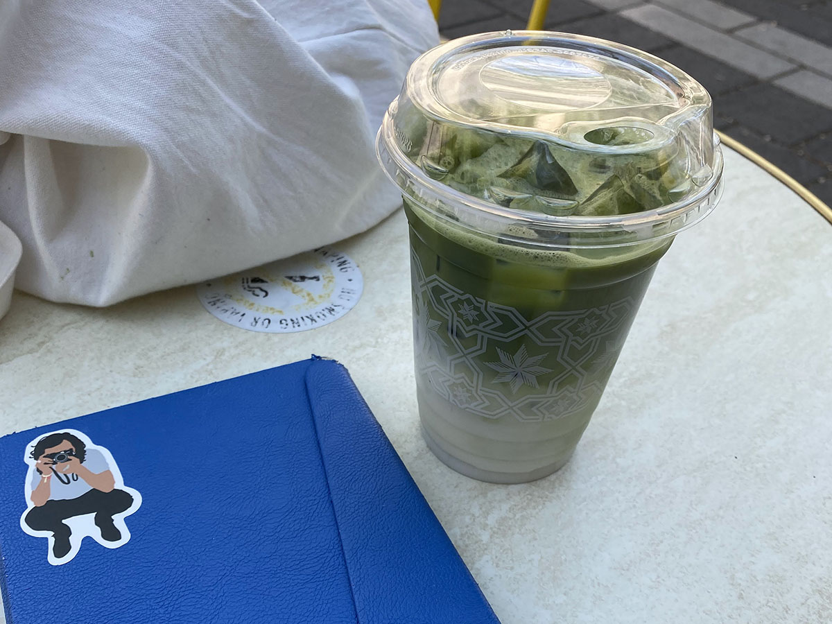 An iced matcha latte and a closed eReader in a blue case on an outdoor table at Balzac's. 