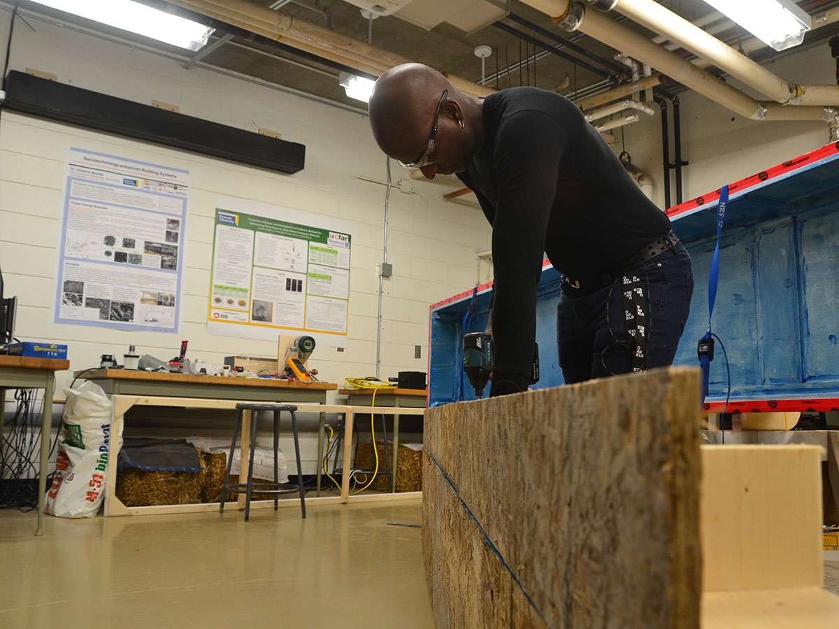 A student uses a drill on a wooden structure in the Building Science Lab.