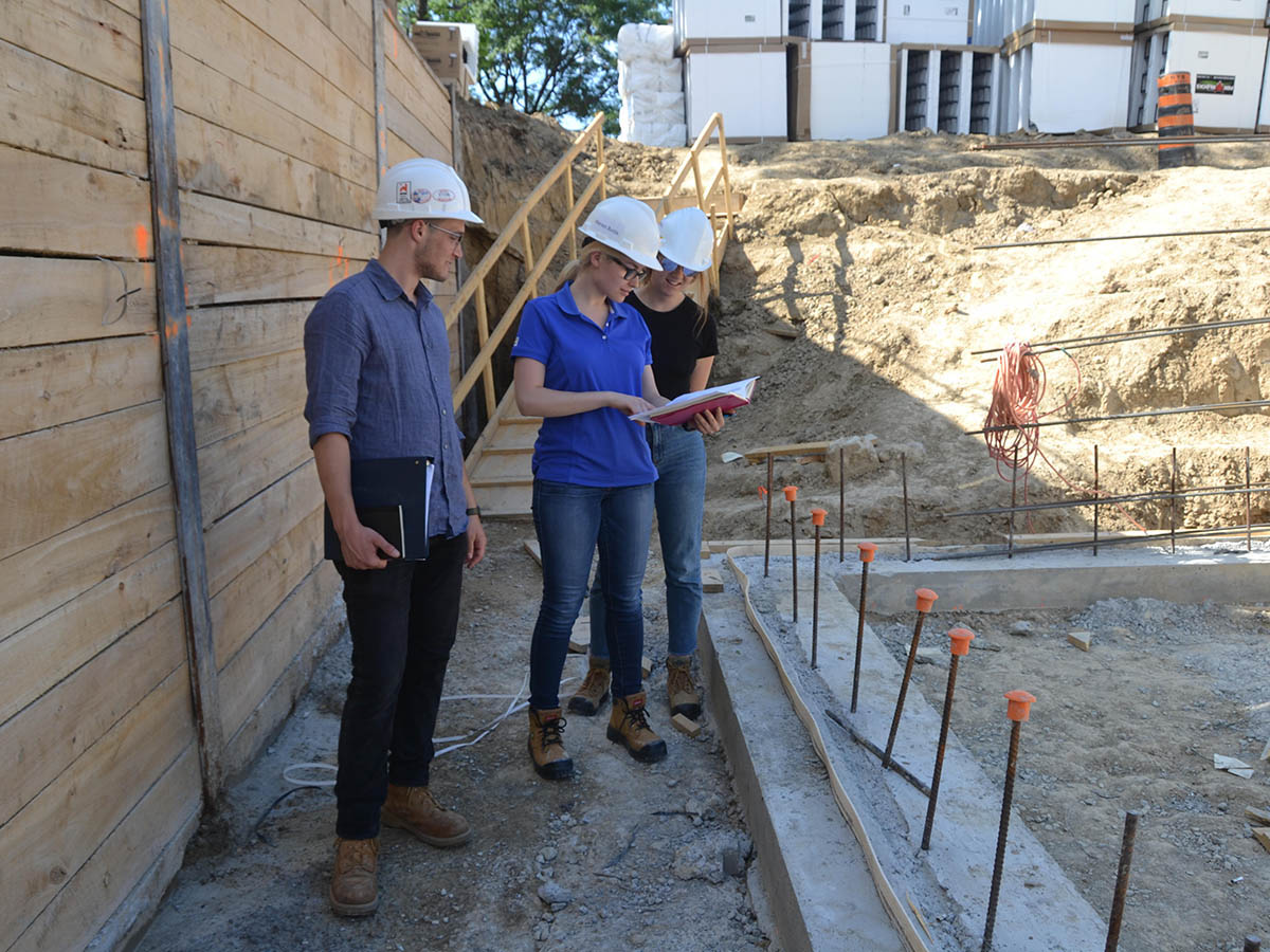 Three students observe building structure at a construction site.