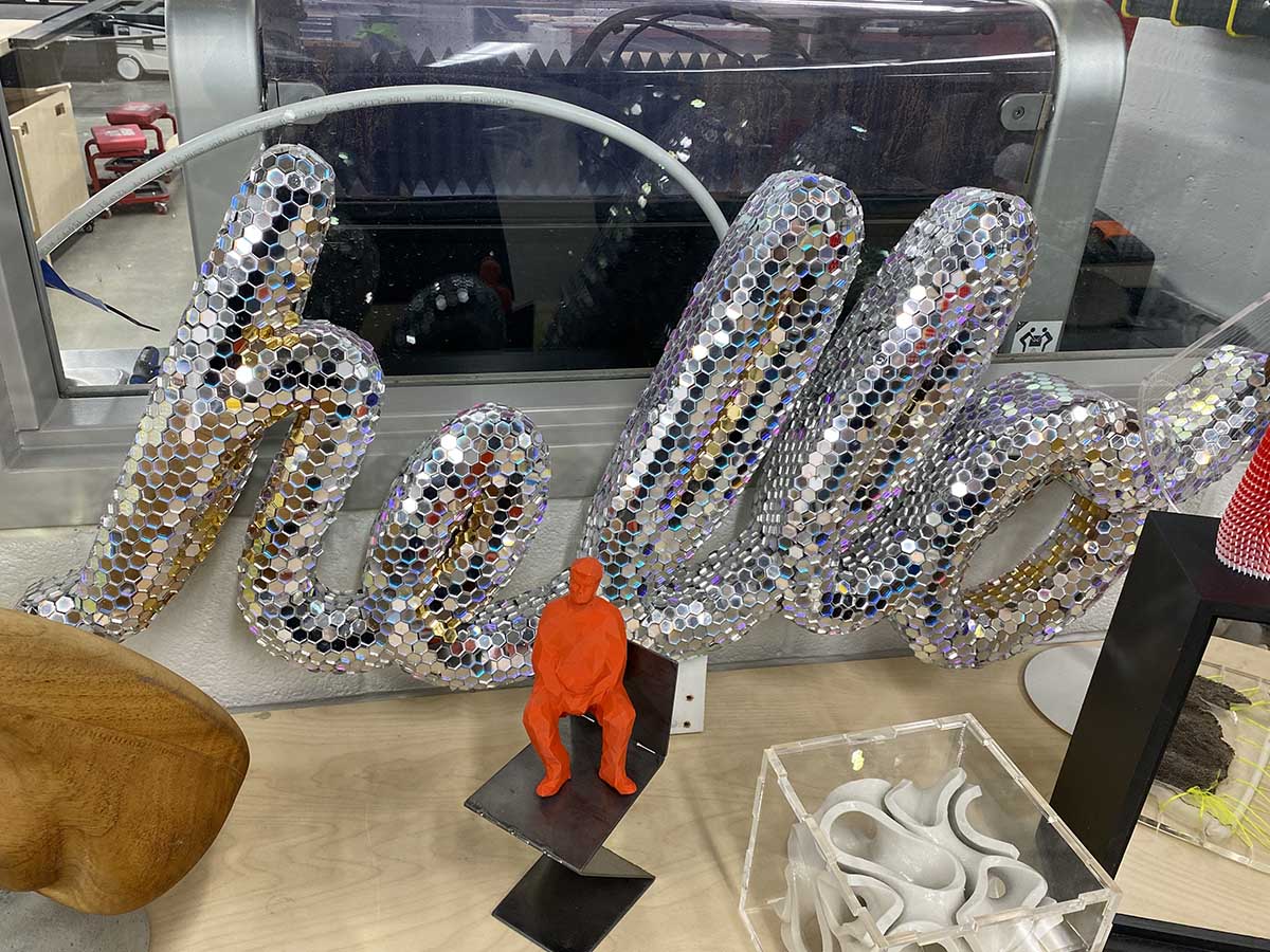 A "hello" sign with "hello" written in cursive and mirrored sequins all over it.