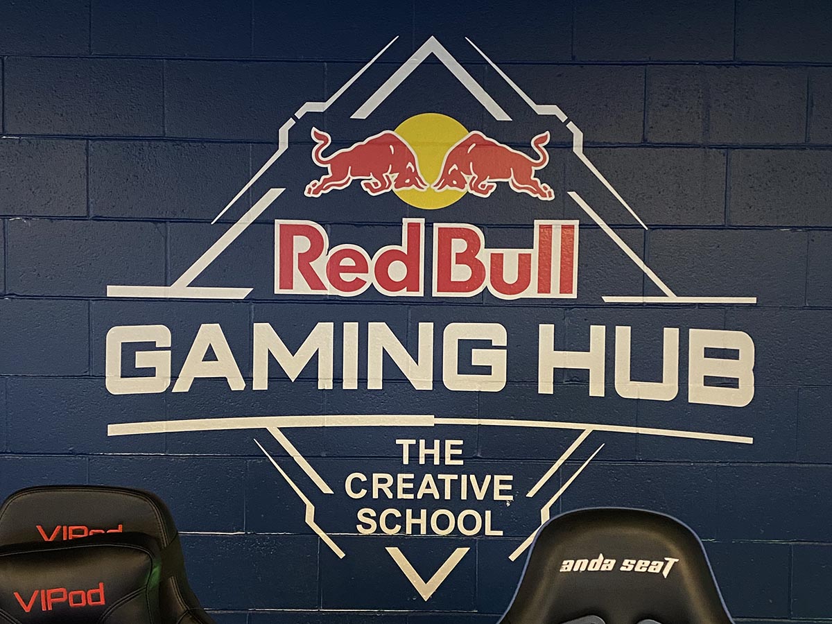 The RedBull Gaming Hub logo on a brick wall painted navy blue with gaming chairs in front.