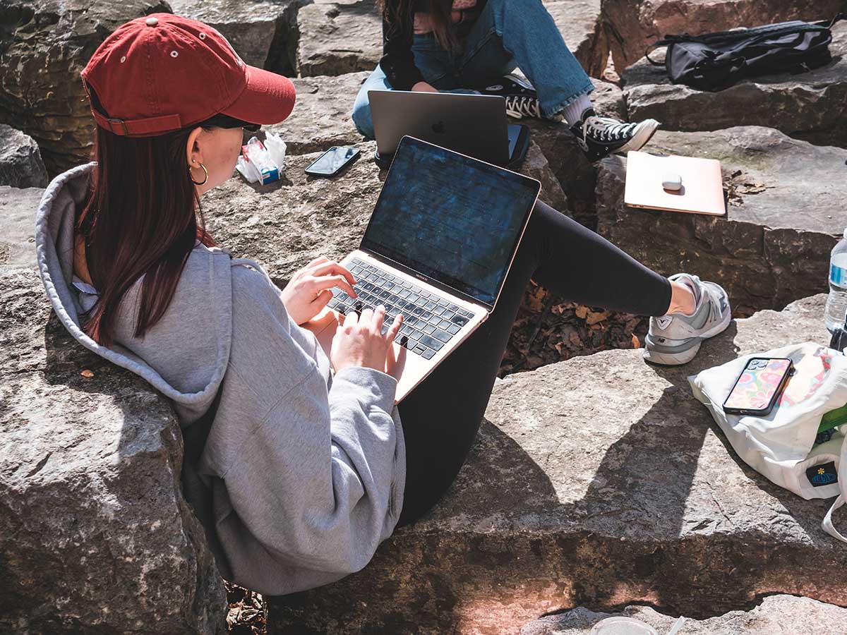 A student works on her laptop while sitting on large stones in Kerr Quad.