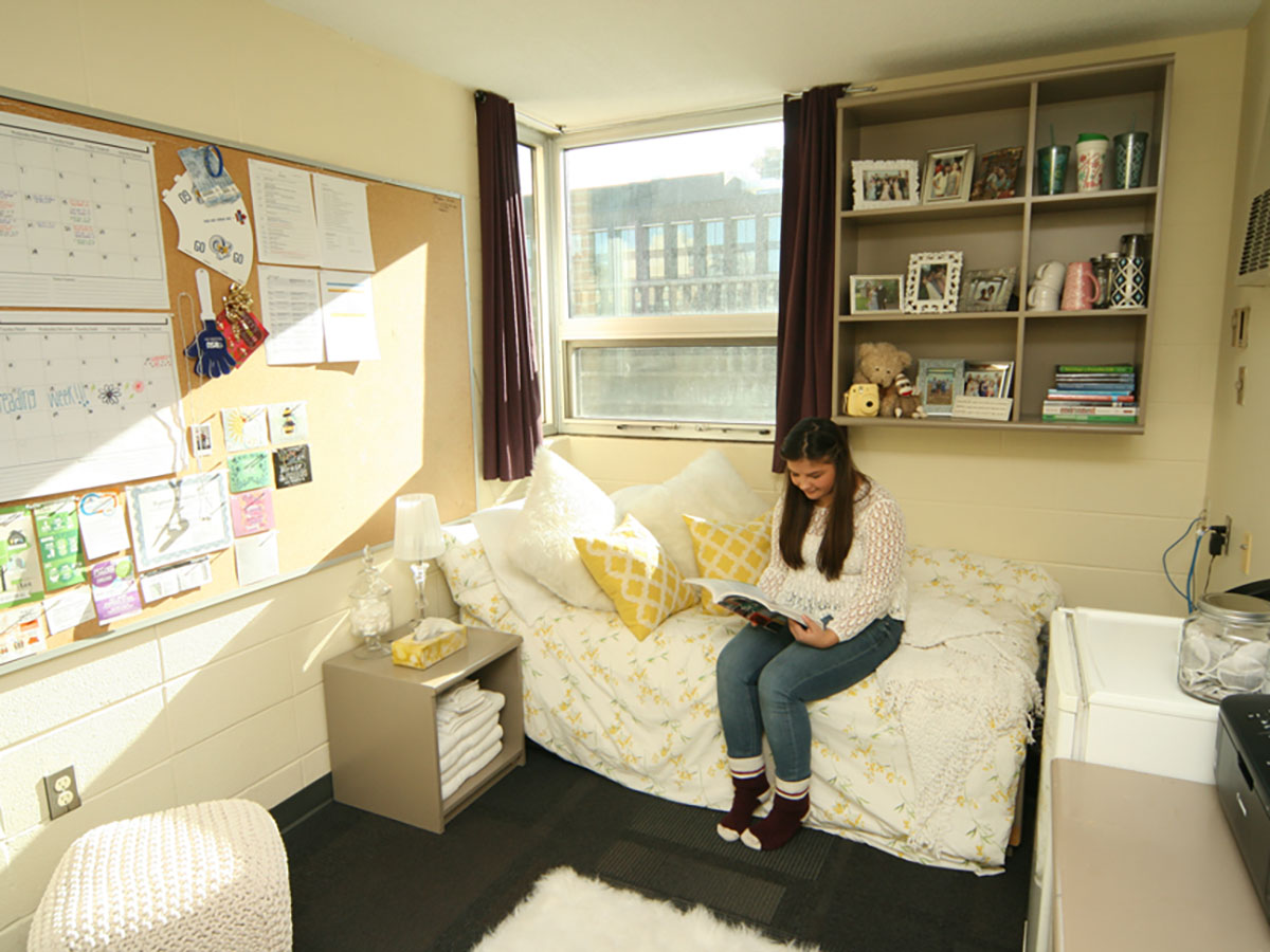 A student reads a magazine on her bed in her dorm room.