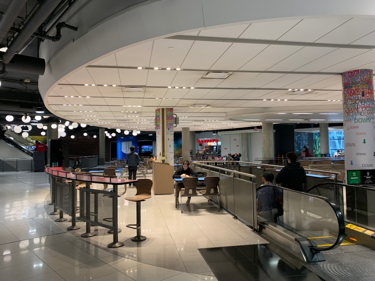 A TMU student sits next to their backpack in the brightly lit food court at 10 Dundas.