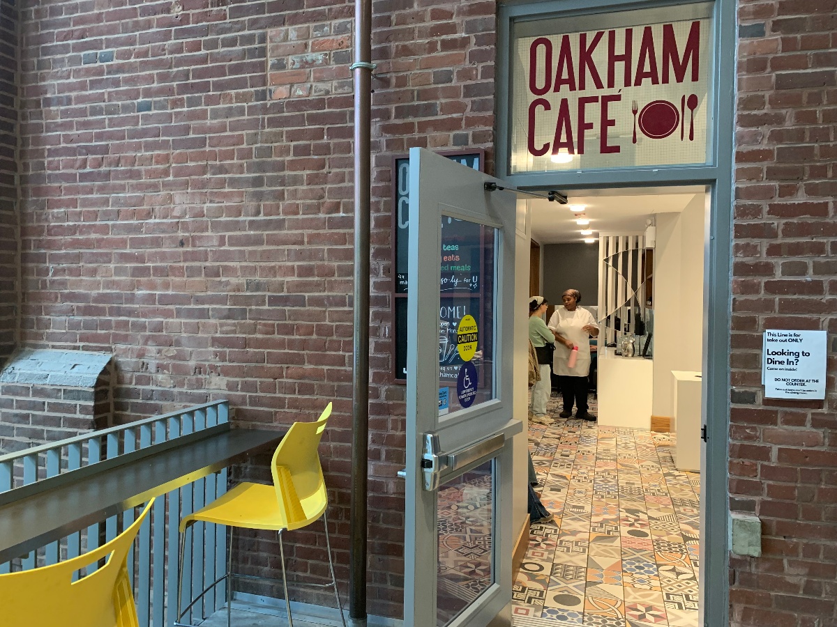 A brick wall surrounds the entrance to Oakham Cafe with empty yellow chairs in front of the doors.