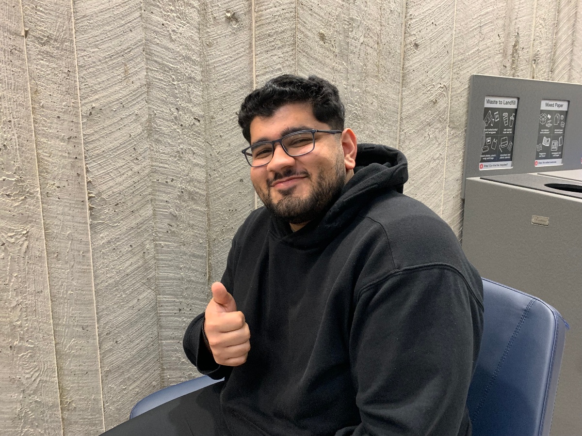 Aman is sitting down smiling and giving a thumbs up.