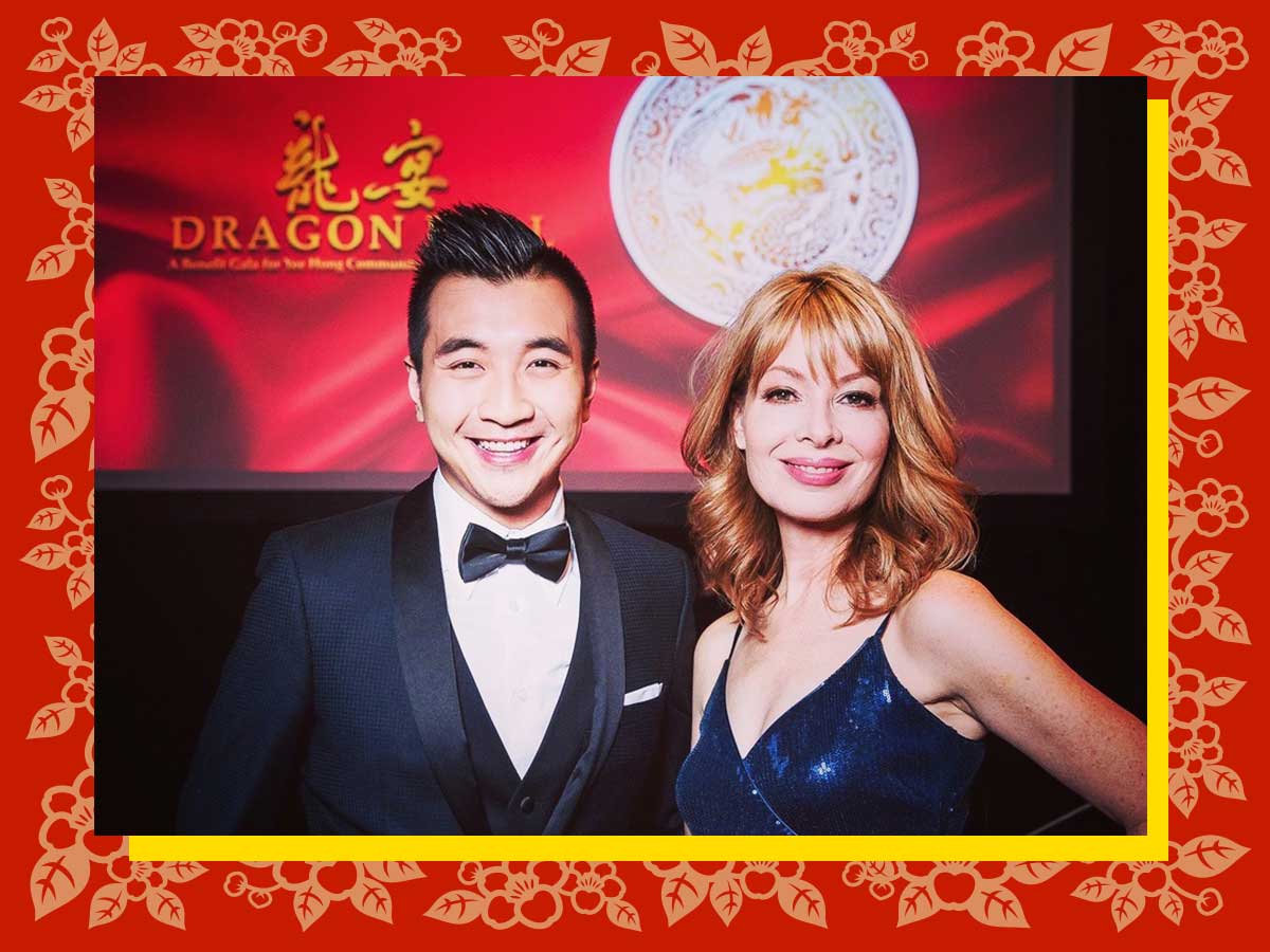 Against a red and gold background identifying the event as the 2019 Yee Hong Dragon Ball fundraiser, Winston Sih is smiling and wearing a dark navy tuxedo standing arm in arm with Cynthia Mulligan dressed in a formal blue dress.