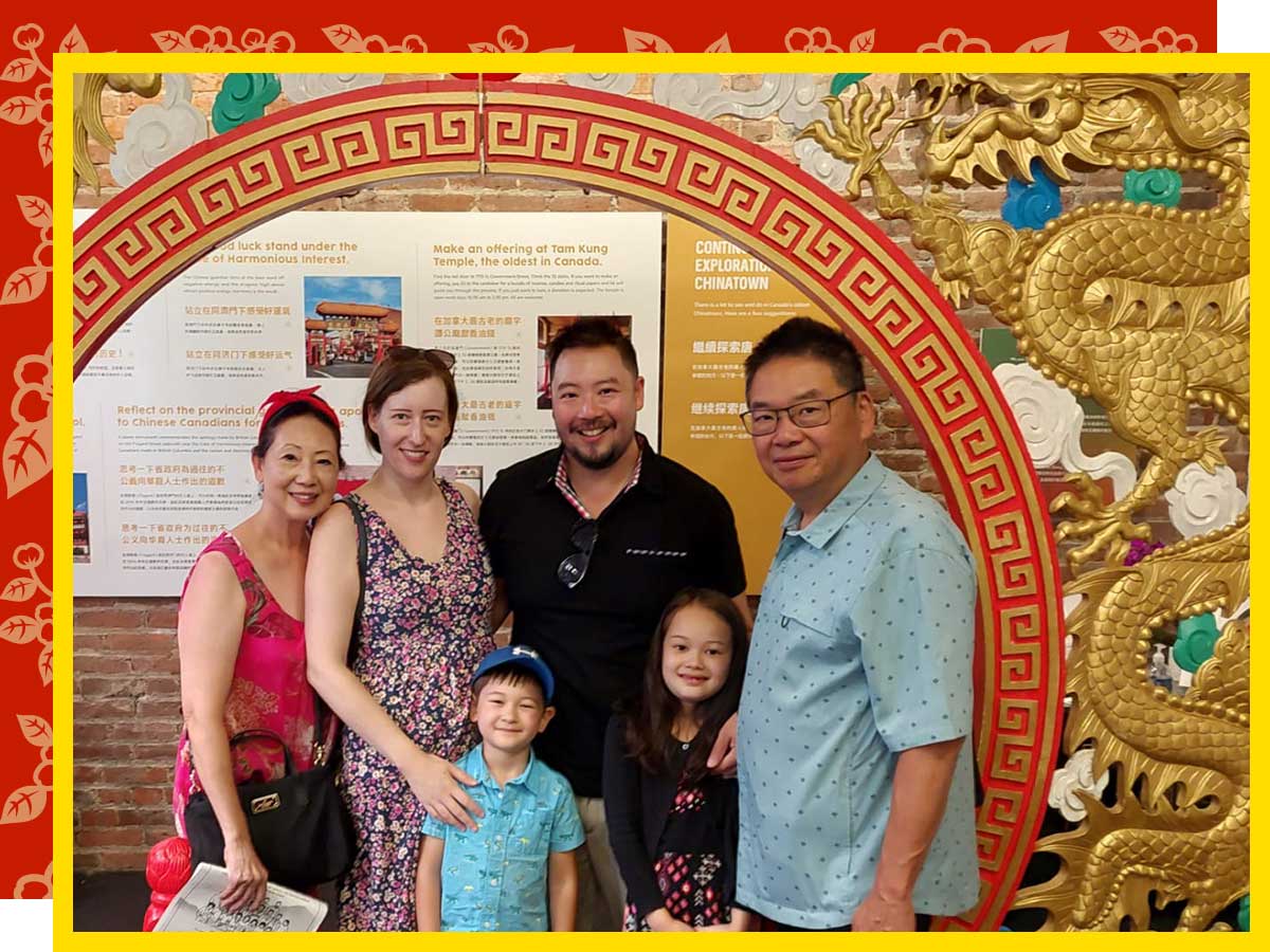 Four adults and two children stand under a red and gold archway decorated with a dragon and phoenix.