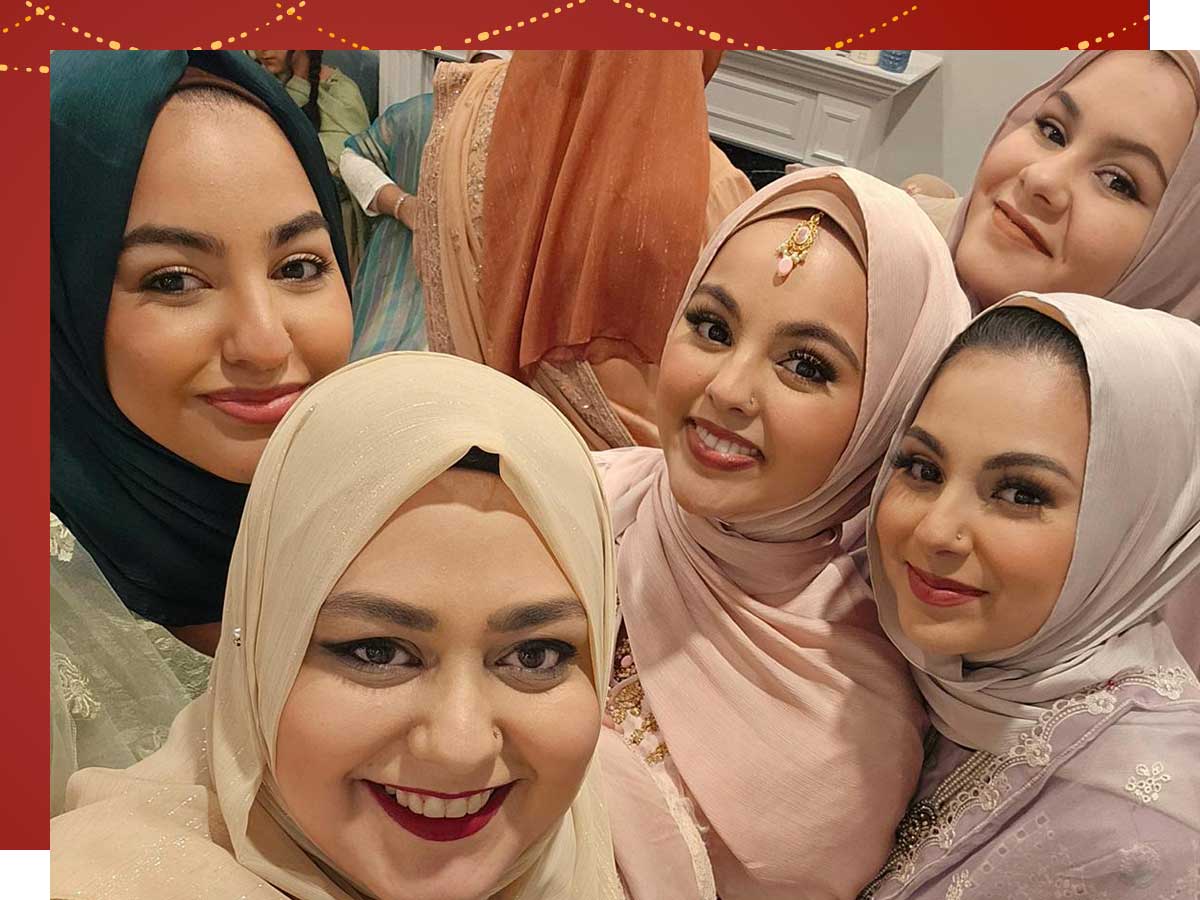 Five young women wearing hijabs and pastel colours smile at the camera