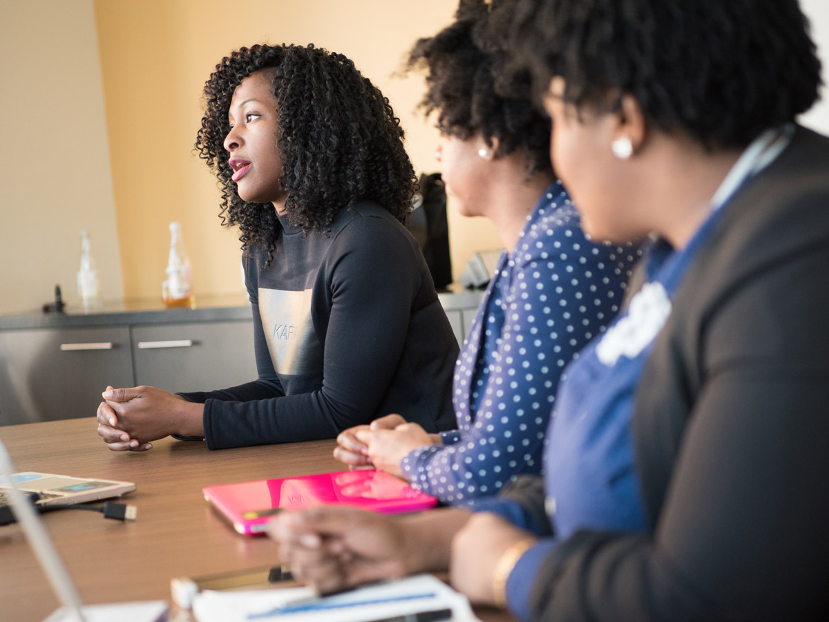 Three Black women talk around a meeting room table.