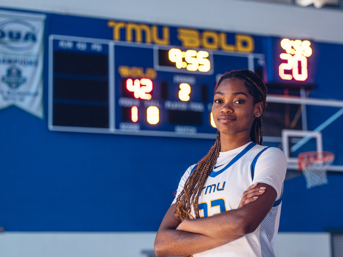 A Black basketball team member in a TMU Bold jersey crosses her arms and smiles confidently.