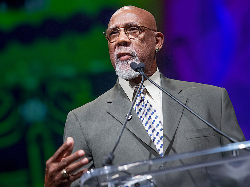 Olympic athlete and activist, Dr. John Carlos, addresses an audience from a podium on stage.