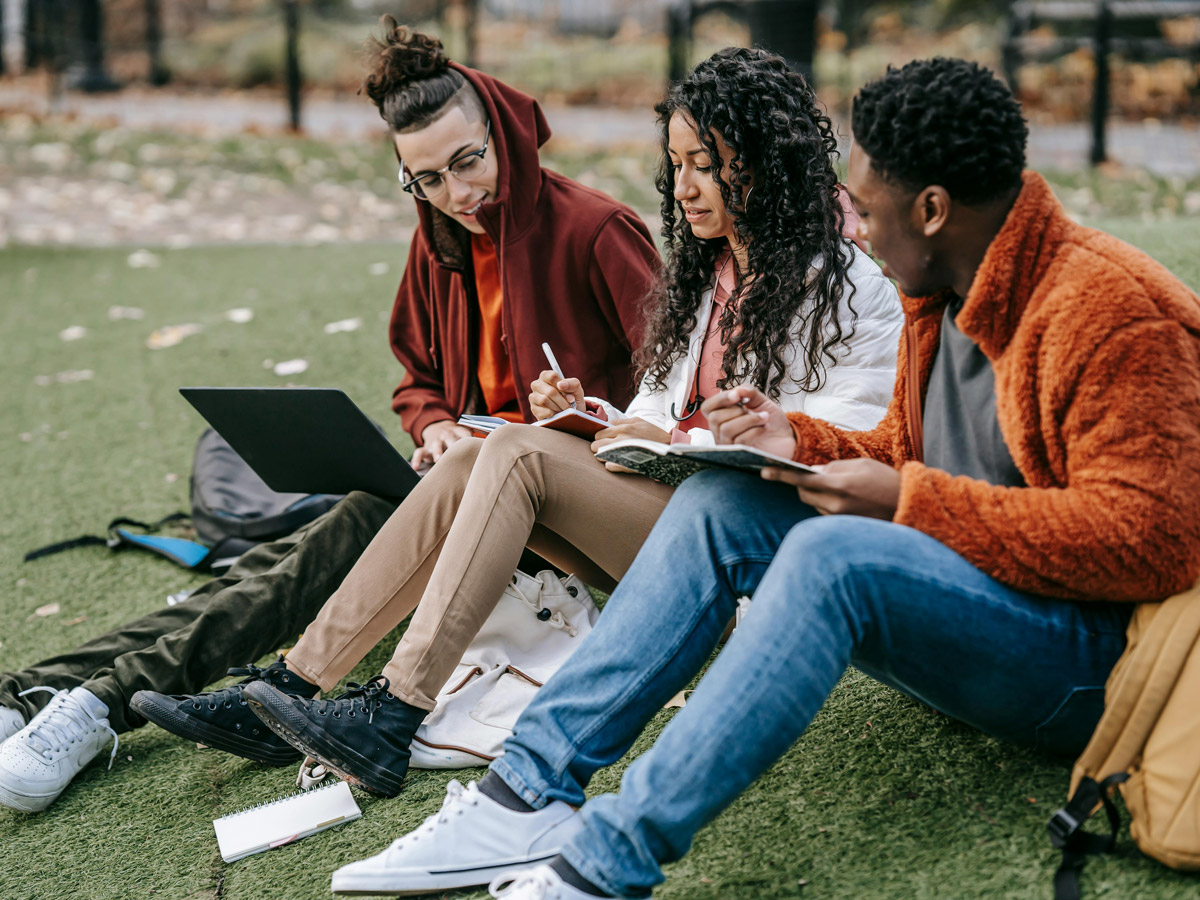 Three students sitting in the grass on an autumn day and working on a project together.