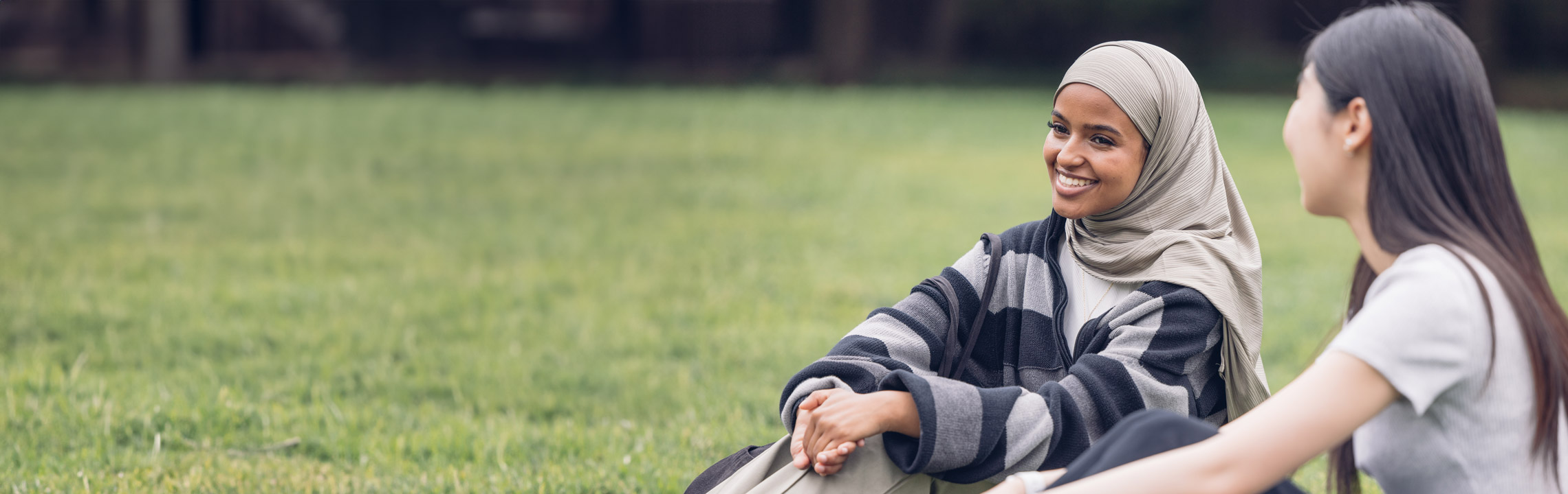 A Black student in a hijab laughs with her friend while sitting in the TMU Quad.