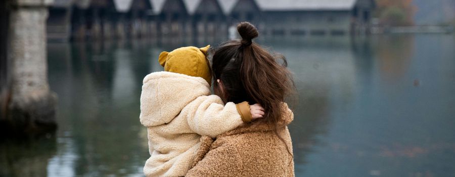 The back of a mother holding her baby while looking over a lake