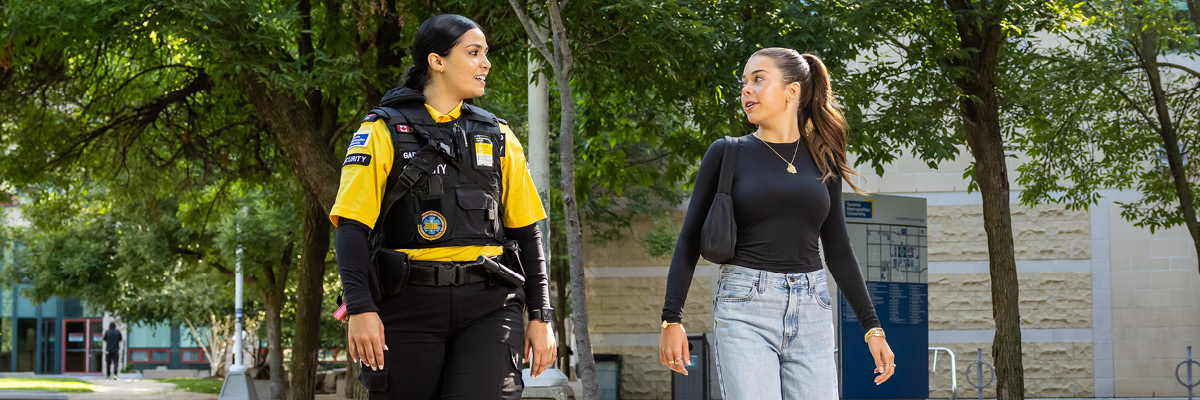 A TMU Security guard in a yellow shirt escorts a student on campus as part of the WalkSafe program.