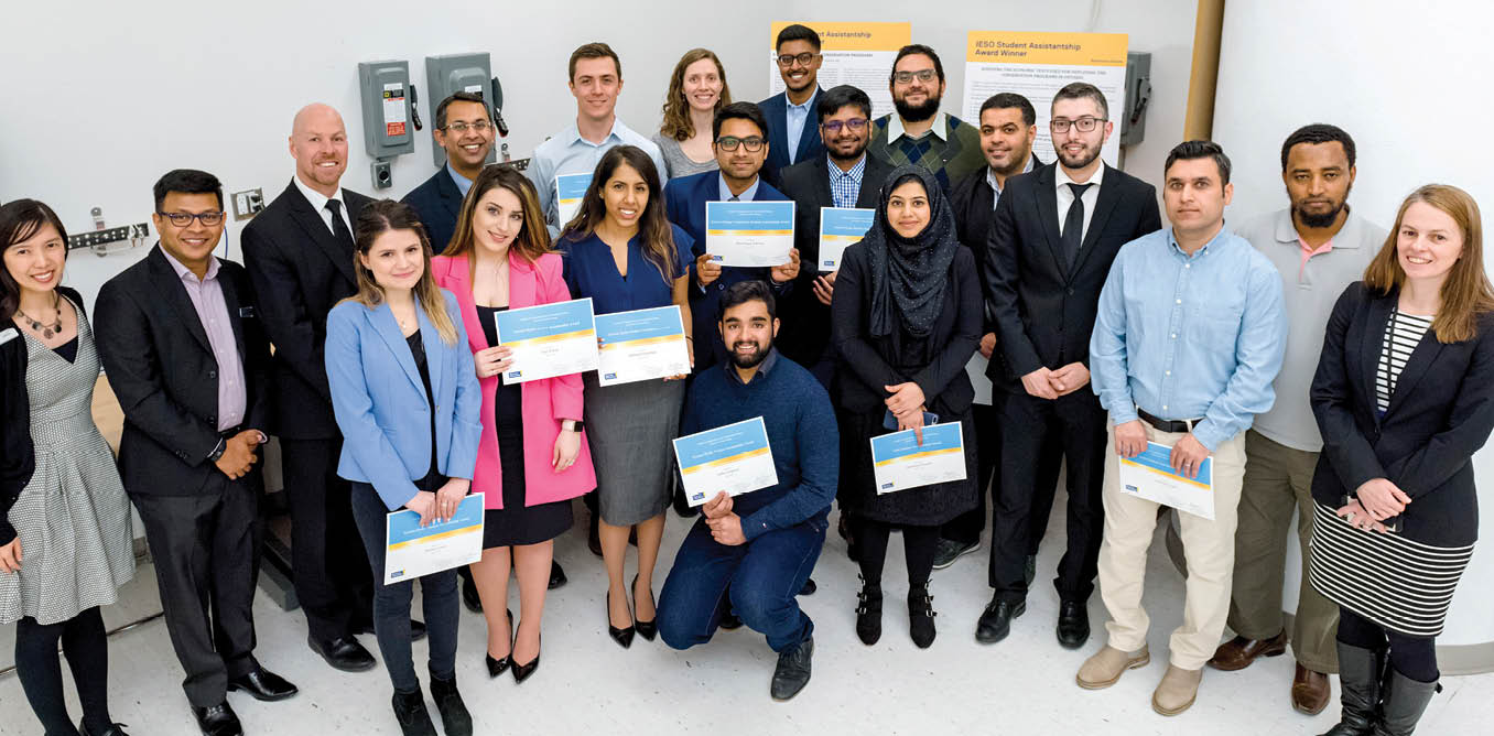 A large group of students and researchers are standing together for a photo. A few of the students are holding award certificates.
