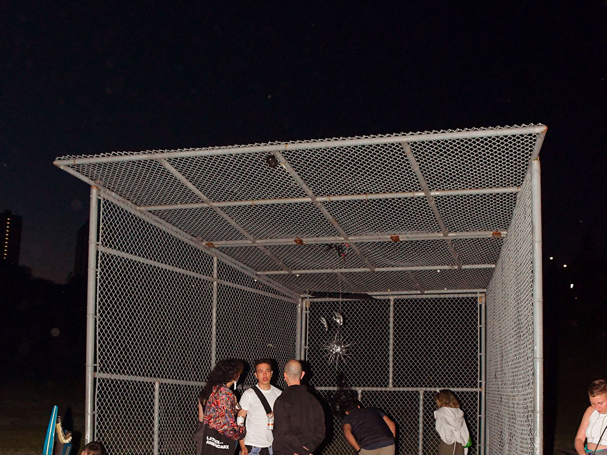 A group of people standing inside a 3-sided chain-link cage at night.