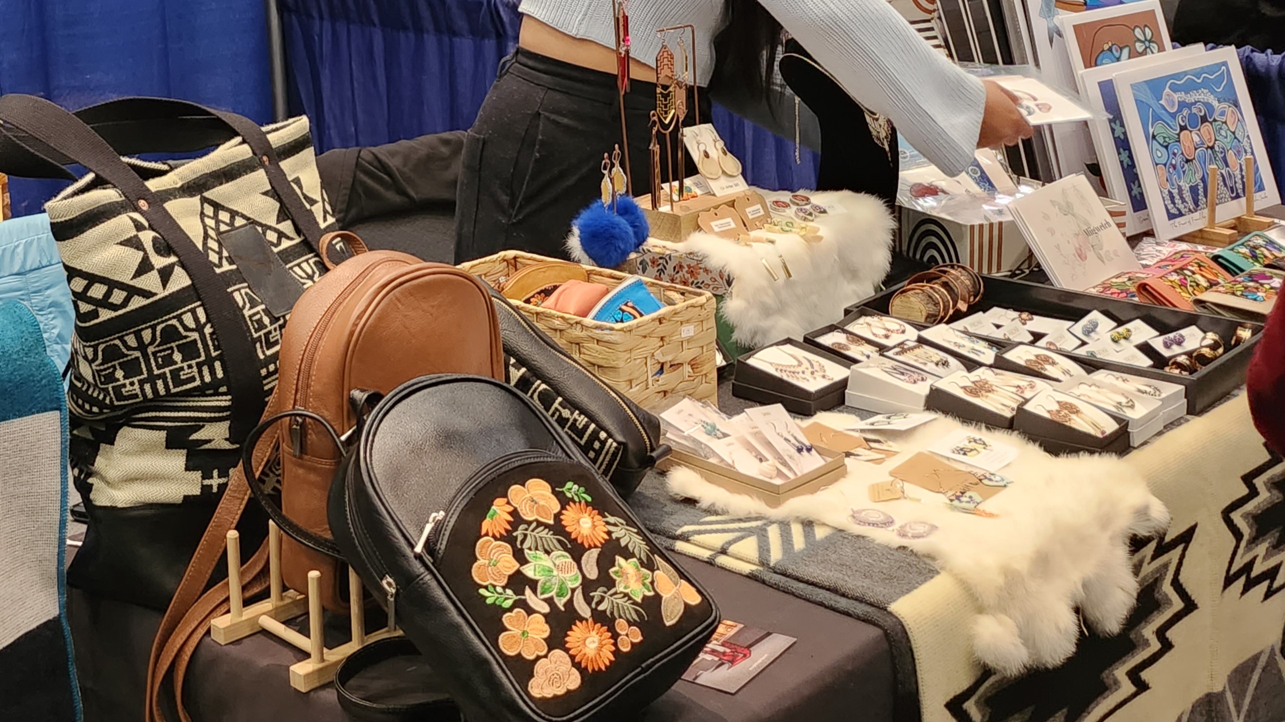 A woman from Pacha Indigenous Art Collection showcases scarves, leather goods, bags, jewelry and art laid out on a table at one of the event’s Indigenous market booths.