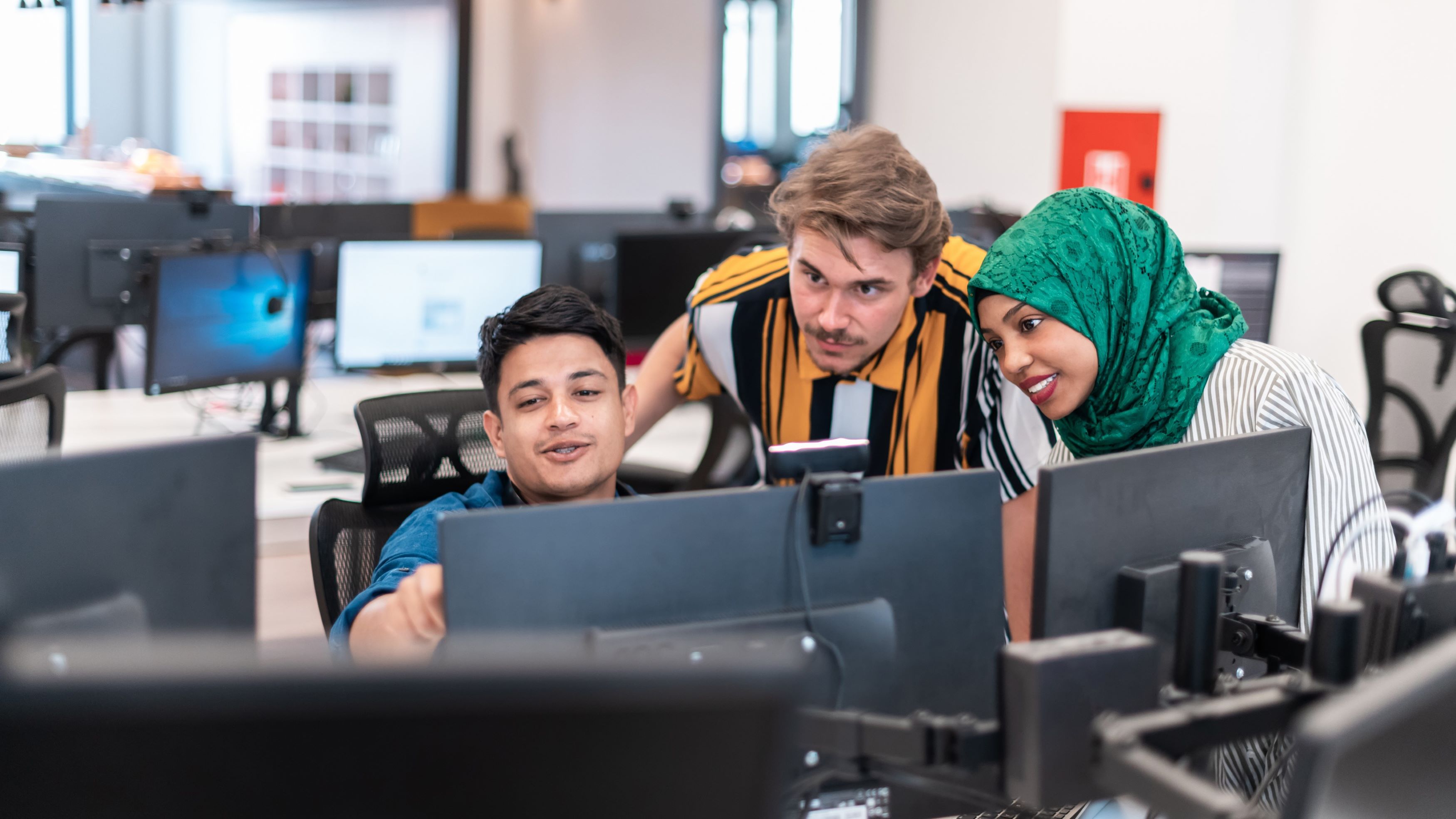 In a shared workspace, a diverse group of people work together at a computer.