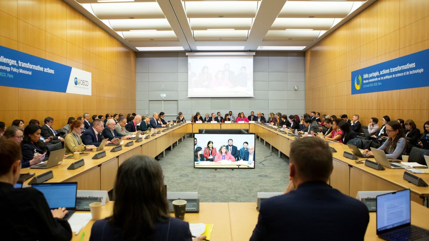 Dozens of professionals exchange insights and ideas in a large boardroom at the Organization for Economic Cooperation and Development headquarters.)