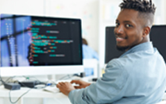young black man looking at camera smiling while coding at a computer