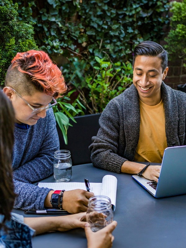 Three people at a table with a notepad and laptop having a discussion.