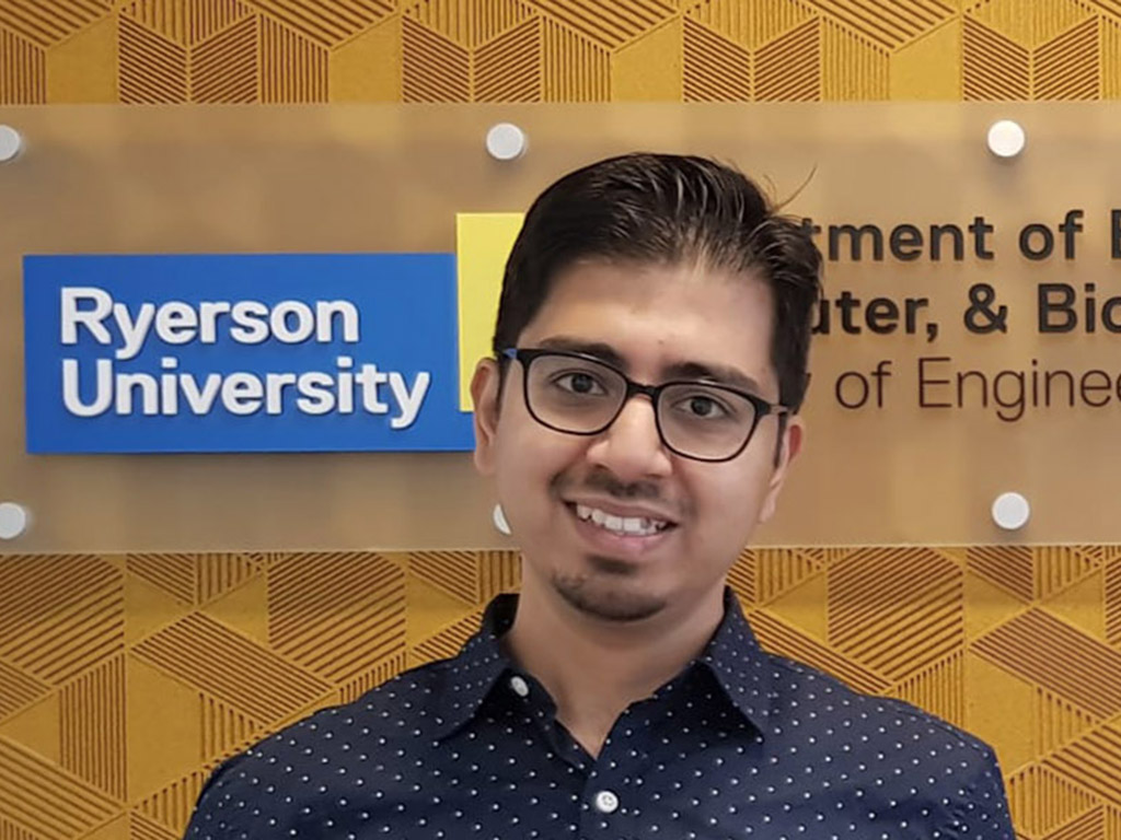 Owais Khan stands in front of an indoor Ryerson University Department of Electrical, Computer & Biomedical Engineering sign