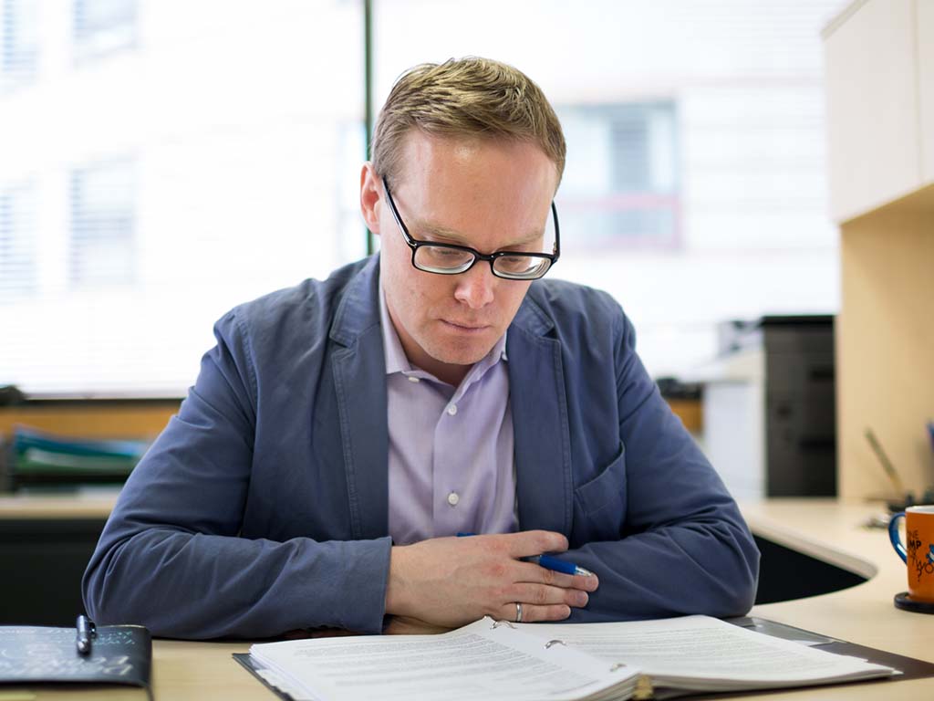 Cory Searcy sits with his arms on a desk looking at pages in an open binder