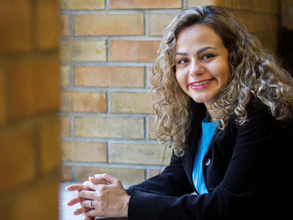 Hadis Zarrin leans on a window well surrounded brick walls smiling at the camera