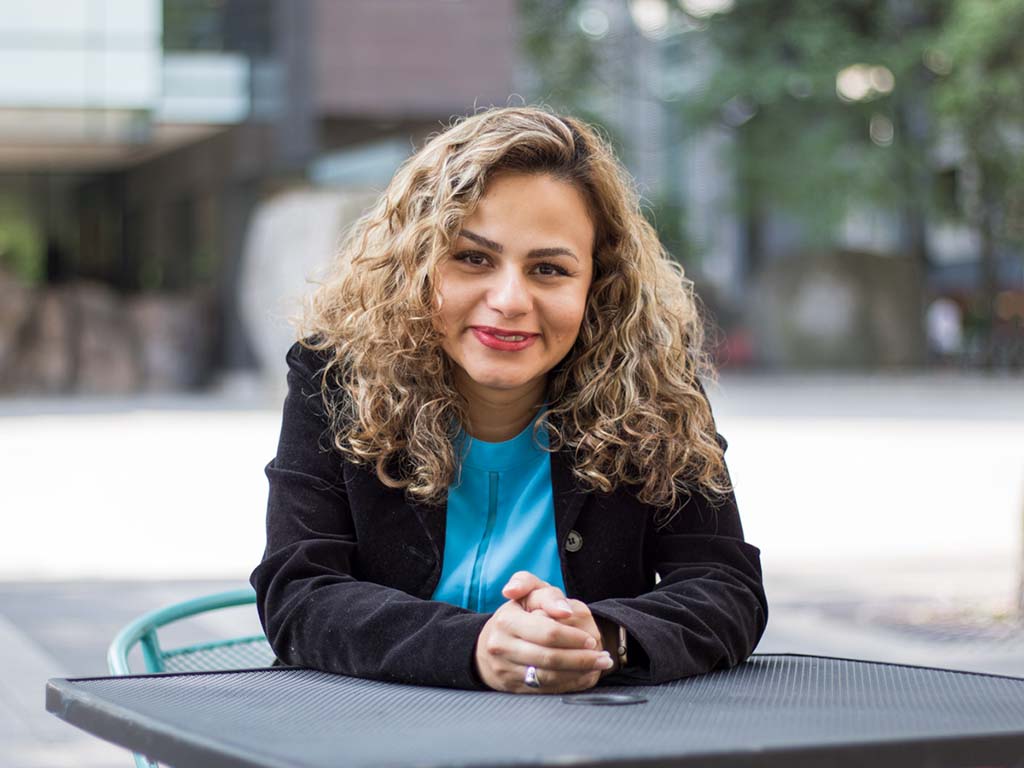 Hadis Zarrin sits with her hands folded on top of a table outside smiling