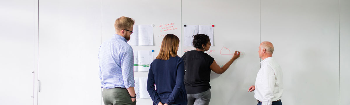 Four diverse faculty members, a mix of ages and backgrounds, collaborating at a whiteboard. 