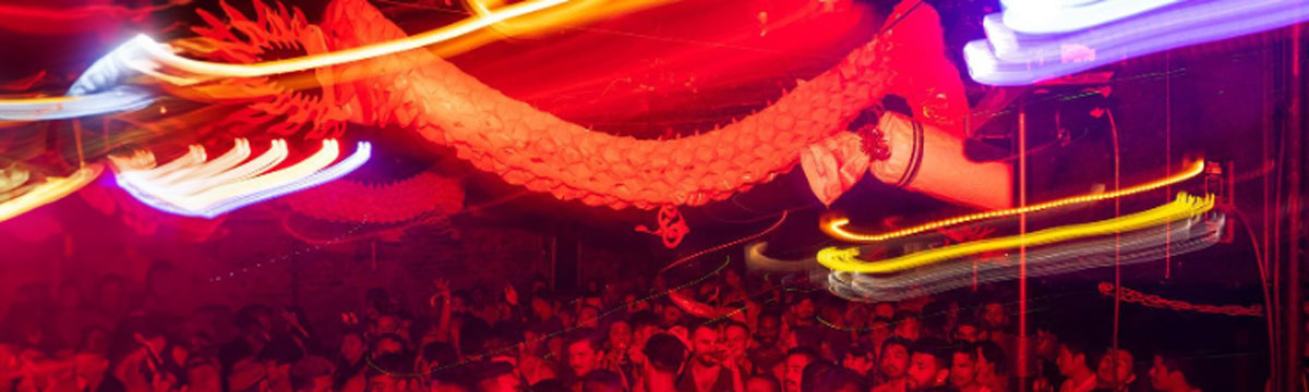 A crowd of people dancing in a neon-lit room with a dragon hanging from the ceiling.