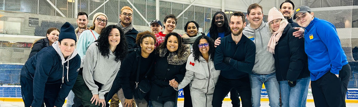 A group of students, faculty and staff smiling on the MAC ice rink. Some of them are wearing skates.