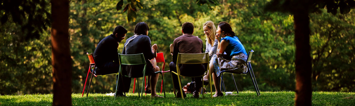 Five people sitting in a circle outside surround by trees on a sunny day